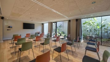 Ein Konferenzraum mit einem Flachbildfernseher, mehreren Stühlen und großen Fenstern mit Pflanzen.