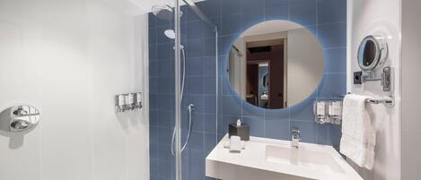 A modern bathroom with a glass-enclosed shower, a white sink, a round mirror, and a towel rack.