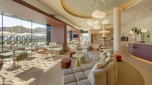 A spacious lounge area with modern furniture, large windows, and a central seating area. - Hampton By Hilton Alicante Airport (Elche)