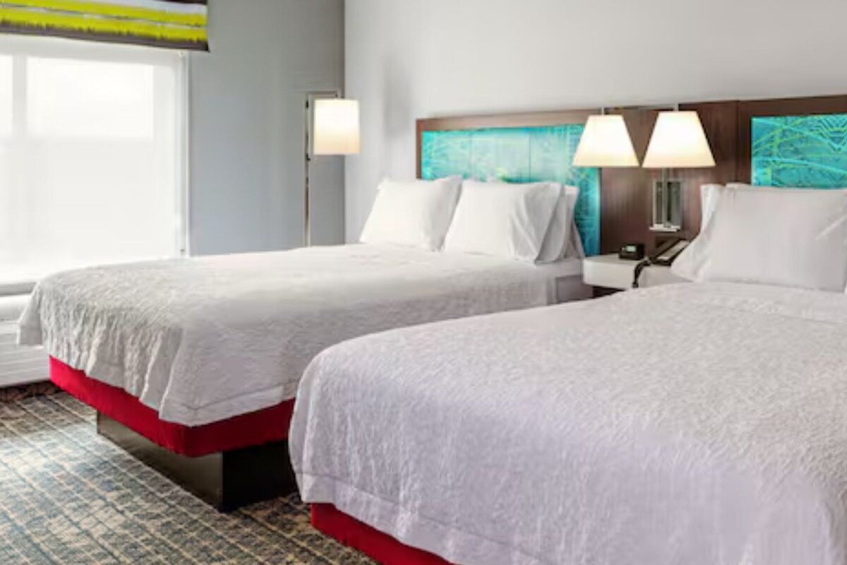 A hotel room with two beds, a nightstand, and a wall with a cityscape mural.