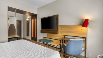 A hotel room with a bed, a desk, a chair, a TV, and a red lamp.