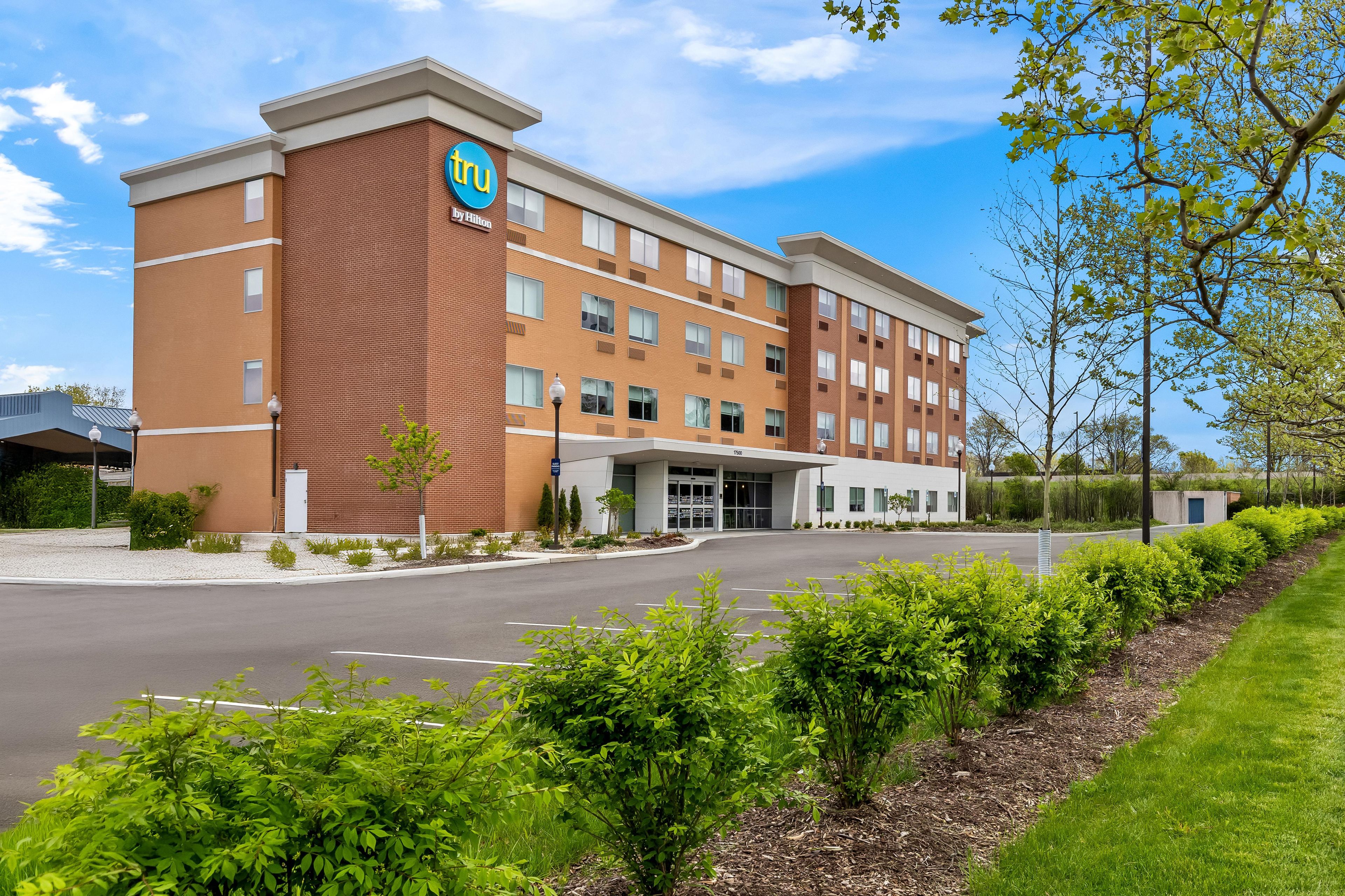 A hotel with a brick facade, a prominent logo, and a parking lot.