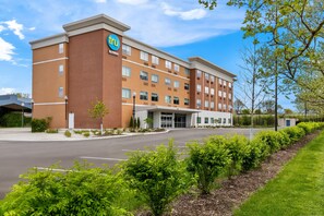 A hotel with a brick facade, a prominent logo, and a parking lot.