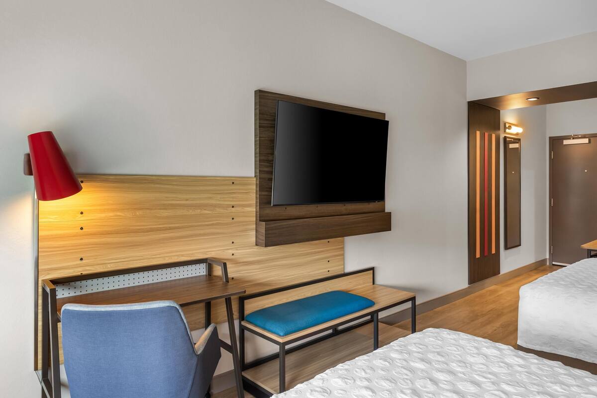 Ein Hotelzimmer mit Bett, Schreibtisch, Stuhl, Wandfernseher und einer roten Lampe.