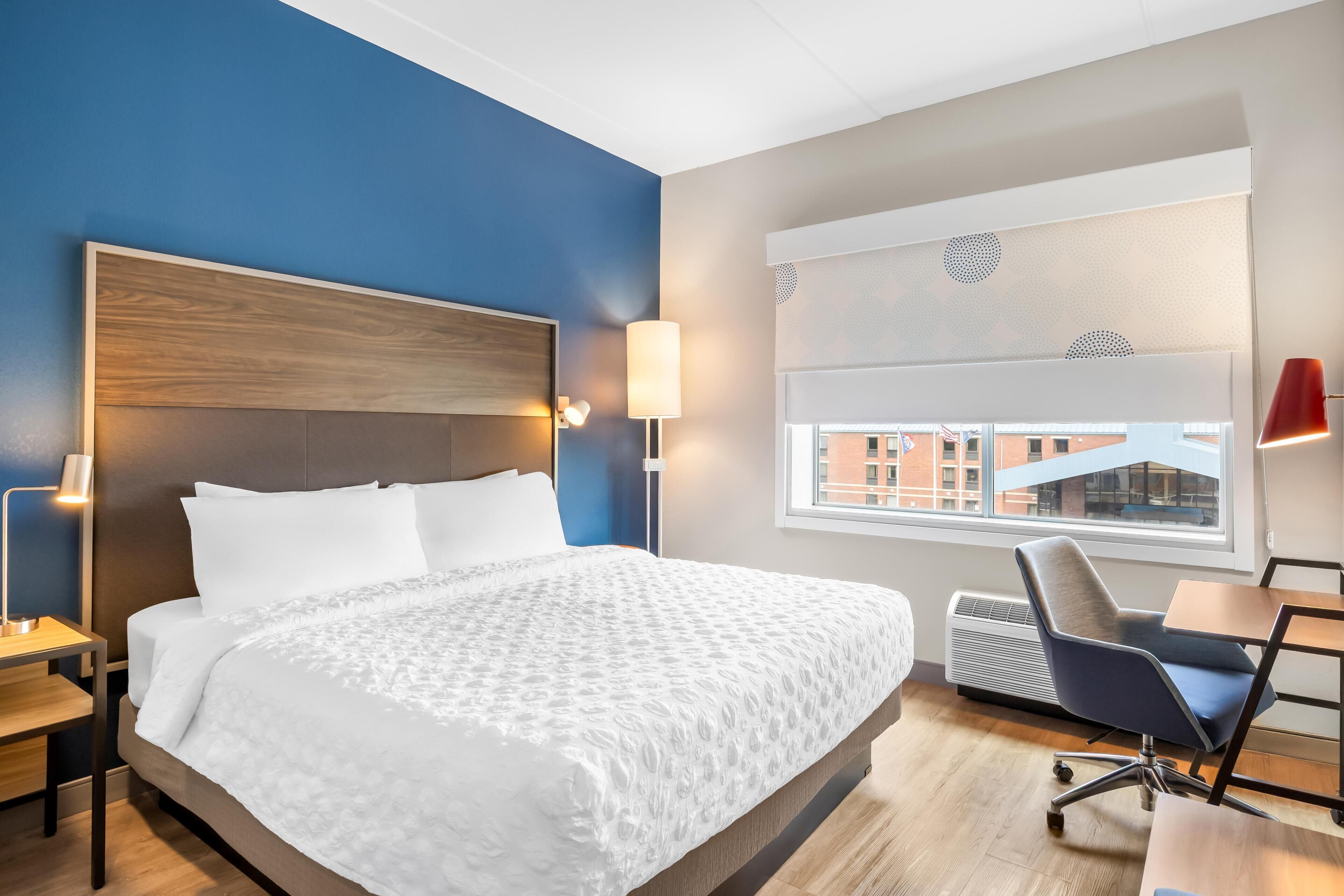 A hotel room with a large bed, bedside lamps, a desk, and a window with a view.