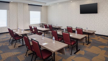 Un salón de conferencias con varias mesas y sillas, un televisor de pantalla plana en la pared y alfombra estampada.
