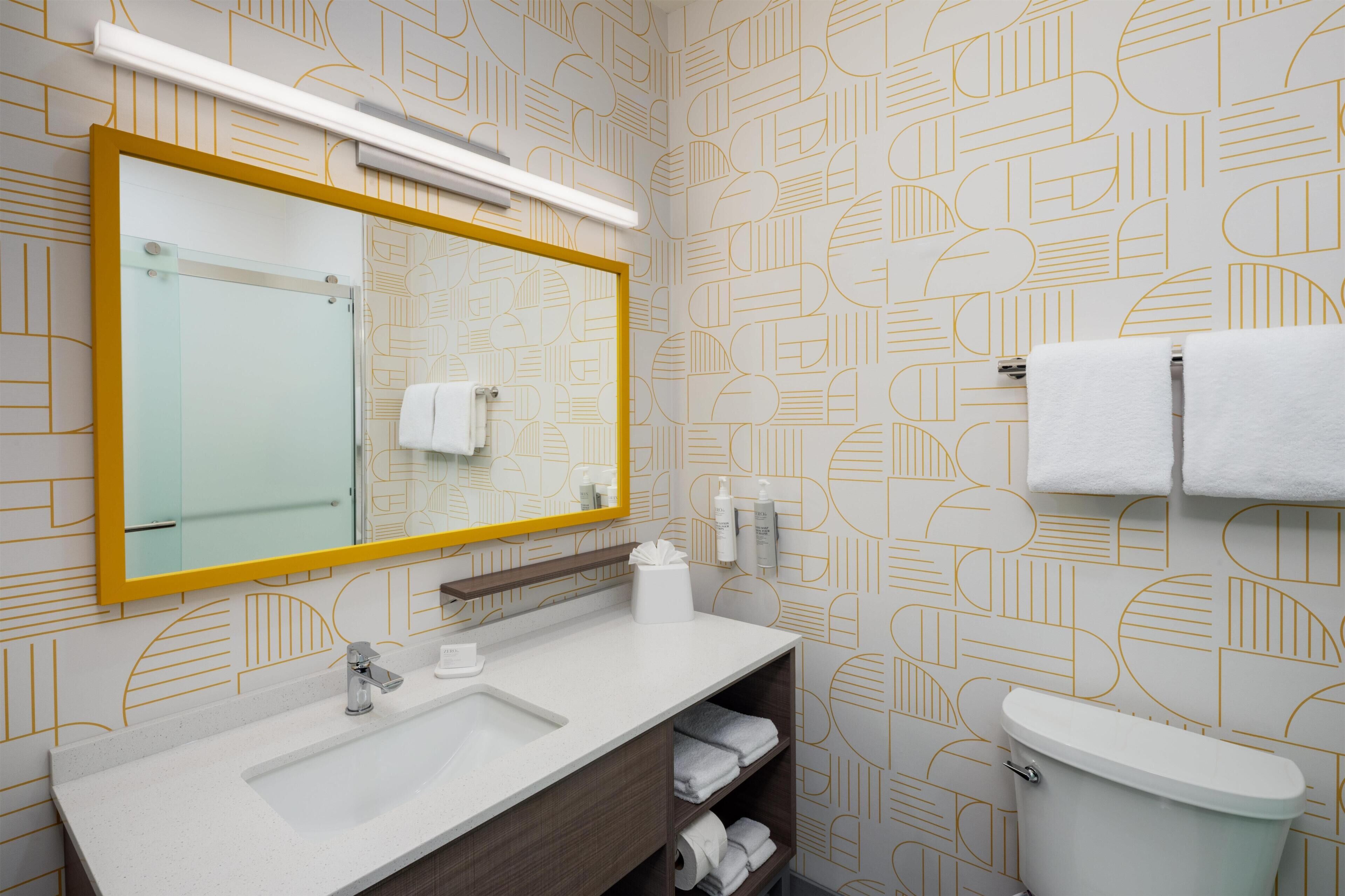 Un baño con un espejo grande, un lavabo, un inodoro y un perchero para toallas.