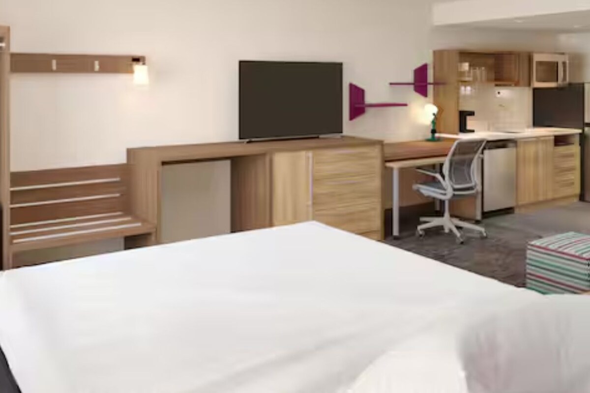 A hotel room with a bed, a desk, a television, a wardrobe, and a suitcase.
