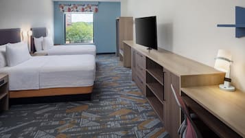 A hotel room with two beds, a flat-screen TV, a desk with a lamp, and a patterned carpet.