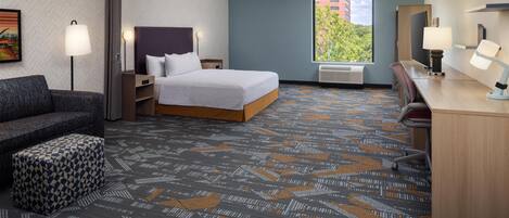 Una habitación de hotel con cama, escritorio, silla, sofá y alfombra estampada.
