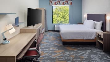 A hotel room with a bed, desk, chair, television, and a window with a view of trees.