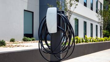 Una estación de carga de Tesla con varios cables conectados, frente a una fachada moderna con ventanas y vegetación.