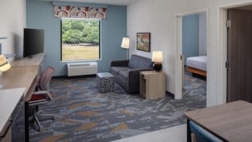 Habitación de hotel compacta con cama, escritorio, silla, sofá, mesita y televisor.