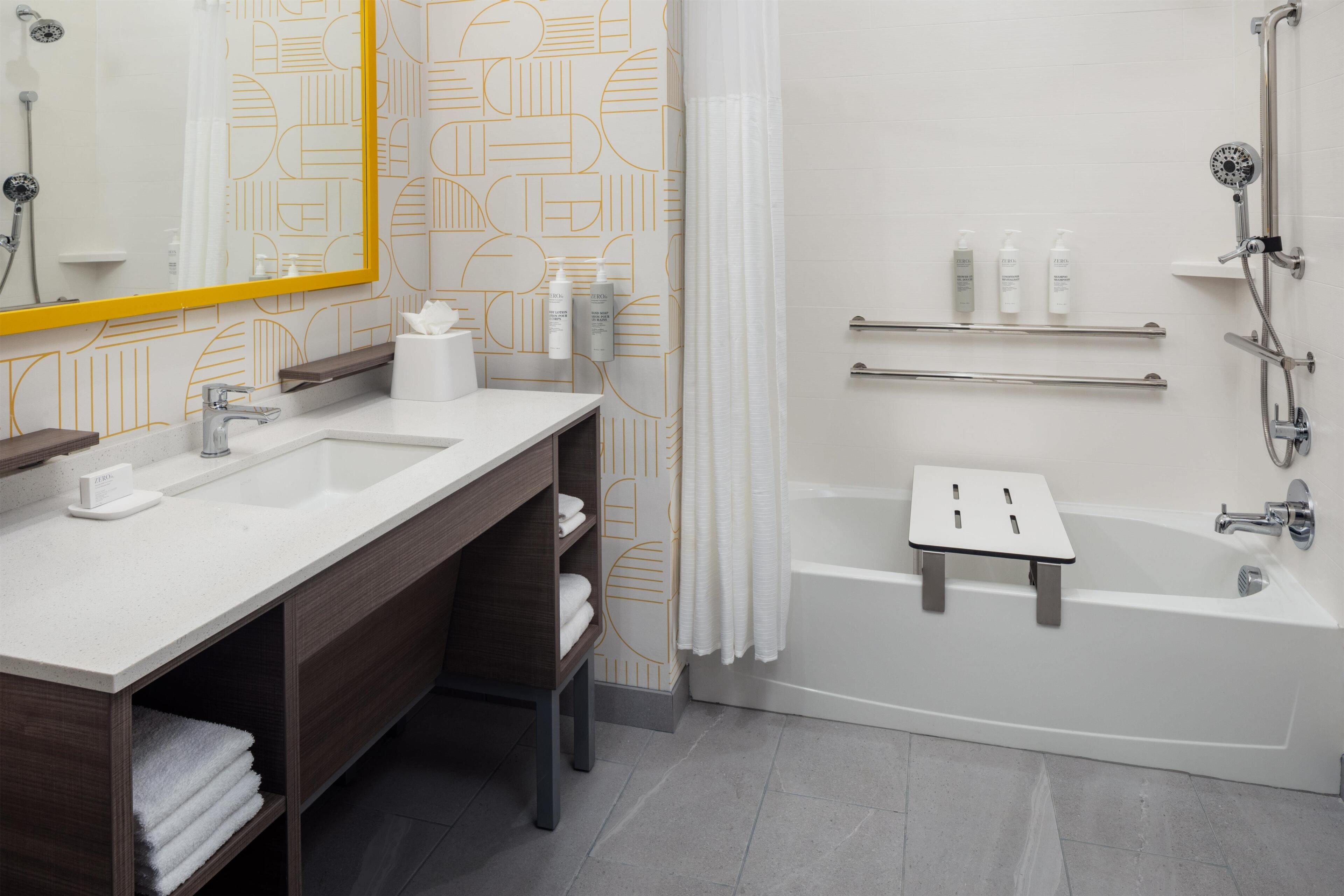 Ein modernes Badezimmer mit einem großen Spiegel, zwei Waschbecken, einer Dusche und einem kleinen Tisch.