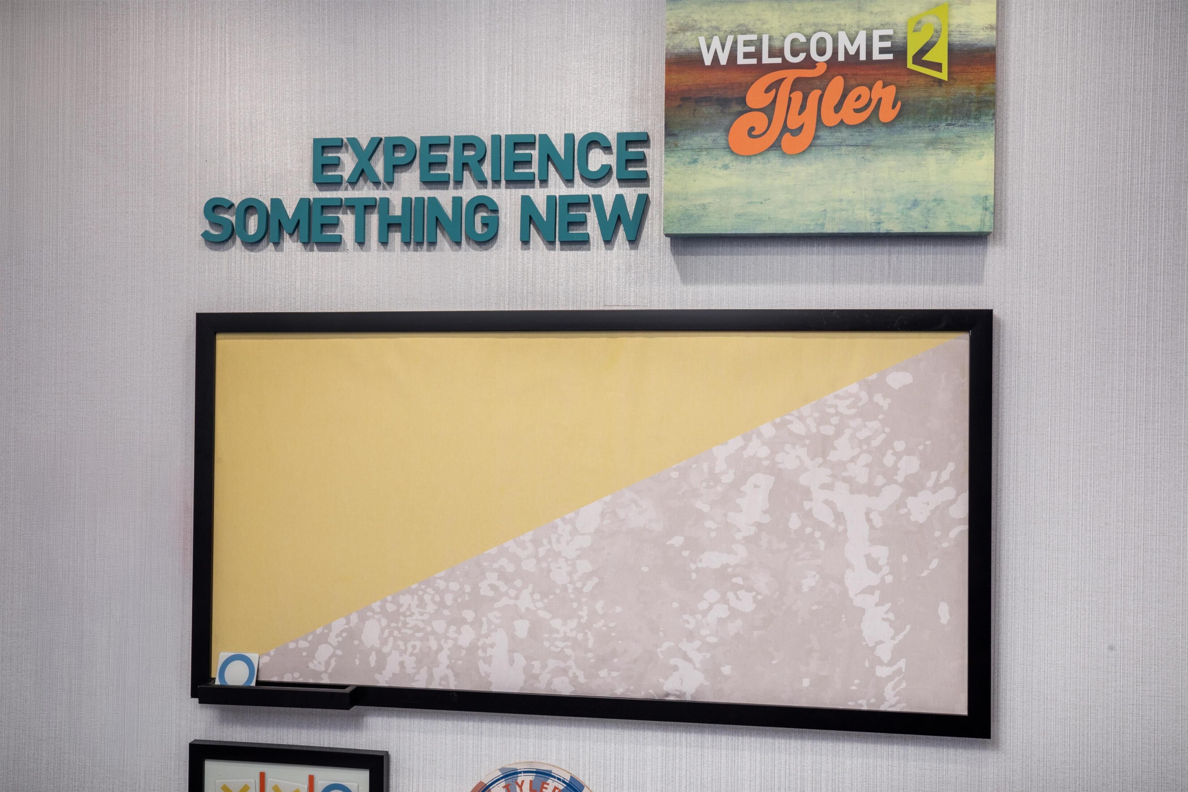 Een muur met een kunstwerk in een lijst en een bordje met de tekst 'WELCOME Tyler'.