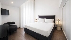 A modern hotel room with a large bed, a flat-screen TV mounted on the wall, a dark armchair, and a bedside table with a lamp. - Maison Michela Sorrento (Sorrento)