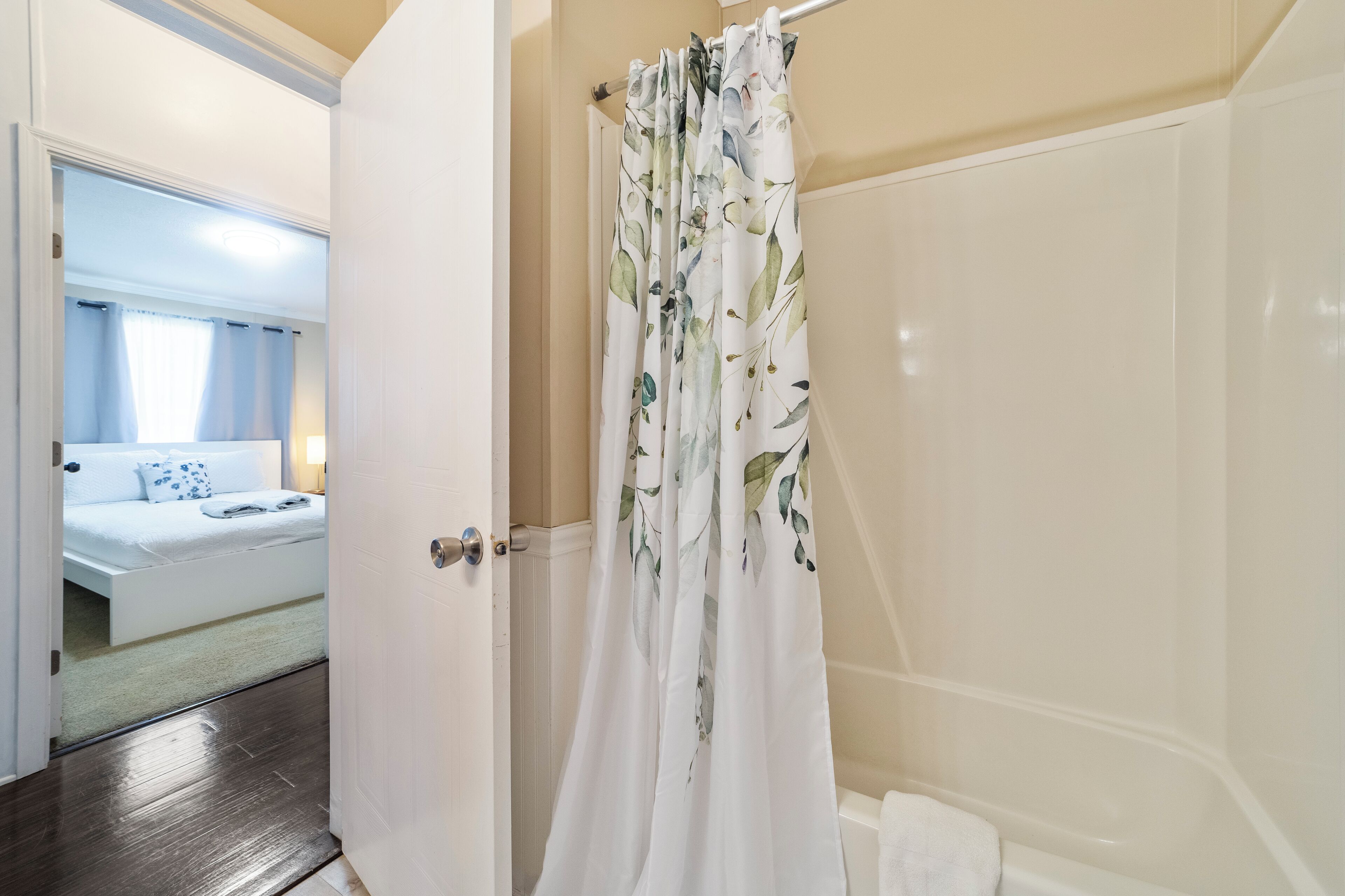 Un baño con cortina de ducha, bañera y puerta que da a un dormitorio.
