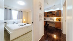 A bedroom with a bed, a nightstand, and a bedside table. There is a window with curtains, a wall clock, and a small shelf with decorative items. The room has a carpeted floor and white walls. - Raceway Retreat, just 12 miles from UF/downtown, relaxing country getaway! (Gainesville)