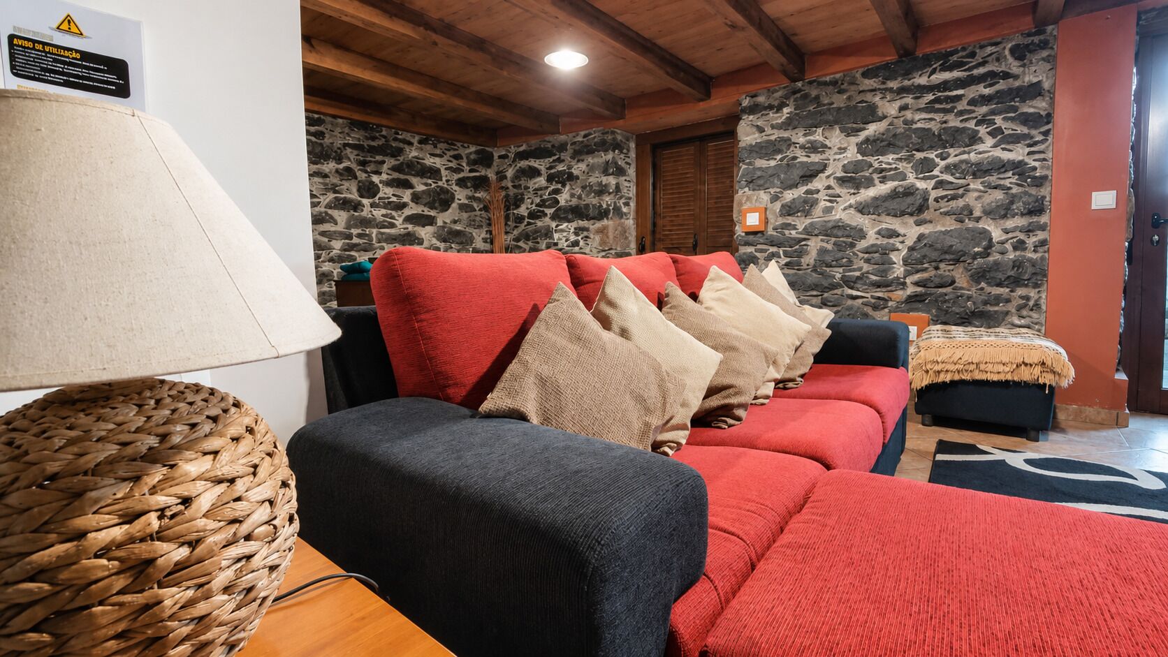 Una habitación acogedora con pared de piedra, un sofá rojo con varios cojines, una cesta tejida y una mesa de madera.