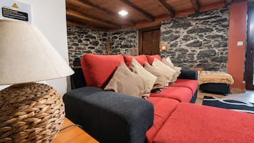 Una habitación acogedora con pared de piedra, un sofá rojo con varios cojines, una cesta tejida y una mesa de madera.