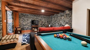 A pool table with billiard balls, a sofa, a television, and a stone wall. - Casa da Achada de Cima (Calheta)