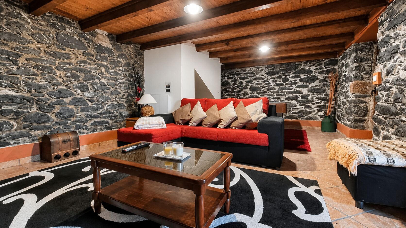 A cozy room with a stone wall, a red sofa with cushions, a wooden coffee table, and a black and white rug.