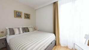 A neatly arranged bedroom with a bed, bedside tables, and a chair. - SURROUNDED BY THE BEST BOUTIQUES, GALLERIES, CAFÉS, AND RESTAURANTS – LE MARAIS (Paris)