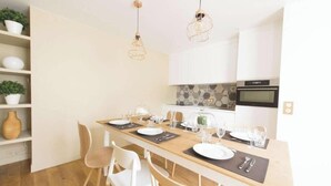 A modern kitchen with white cabinets, a wooden dining table set for four, and a built-in oven. - SURROUNDED BY THE BEST BOUTIQUES, GALLERIES, CAFÉS, AND RESTAURANTS – LE MARAIS (Paris)
