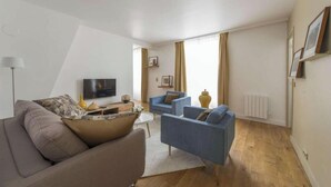 A modern living room with a sofa, a blue armchair, a coffee table, and a TV. - SURROUNDED BY THE BEST BOUTIQUES, GALLERIES, CAFÉS, AND RESTAURANTS – LE MARAIS (Paris)