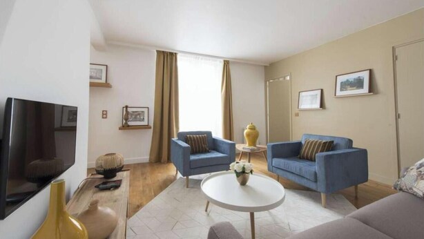 A modern living room with a flat-screen TV, two blue armchairs, a round coffee table, and a sofa. - SURROUNDED BY THE BEST BOUTIQUES, GALLERIES, CAFÉS, AND RESTAURANTS – LE MARAIS (Paris)