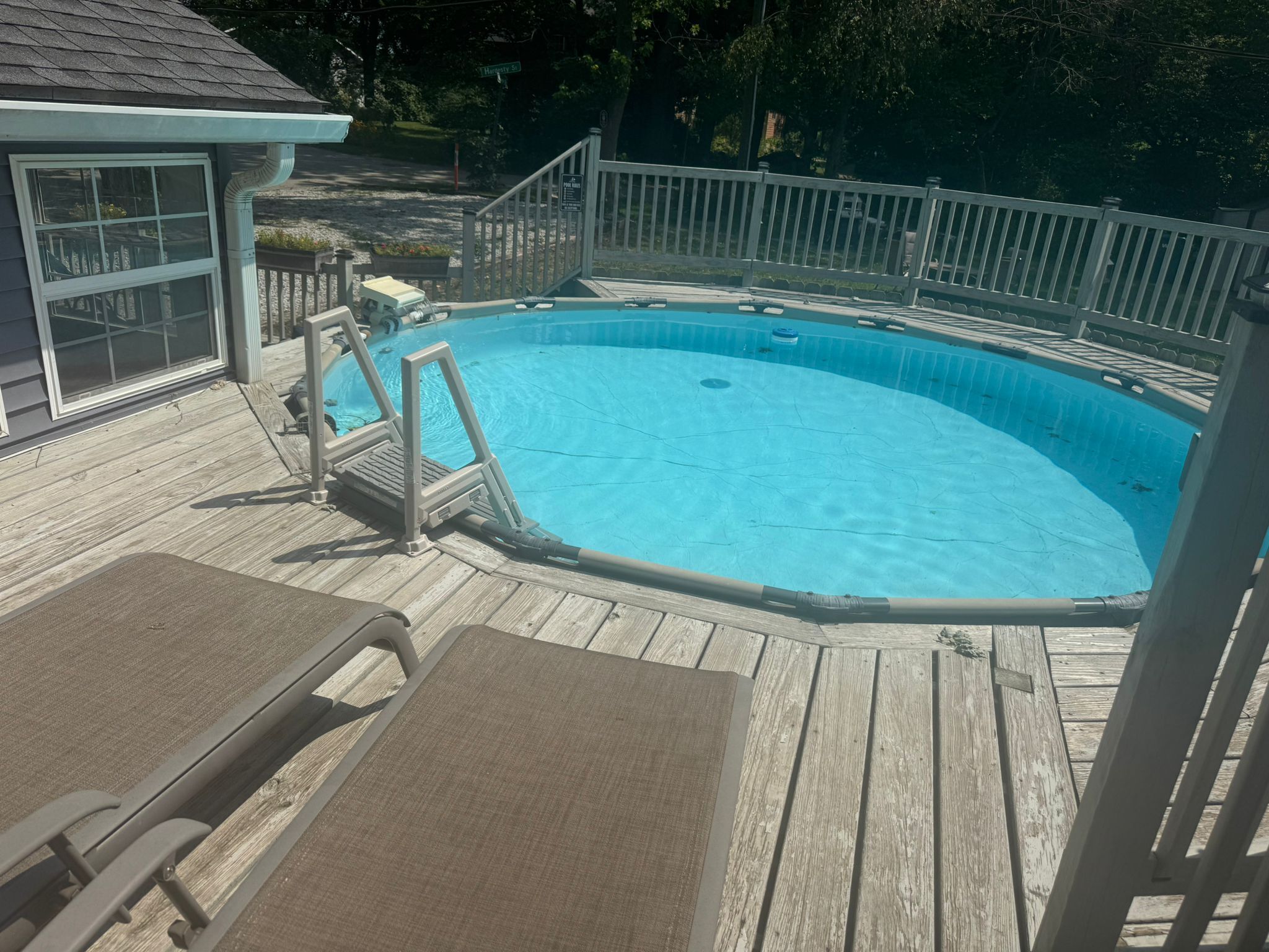 Una piscina con muelle de madera, una escalera y una zona cubierta con sillas.