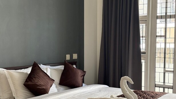 A hotel room with a neatly made bed, a swan-shaped pillow, and a window with a view of buildings.