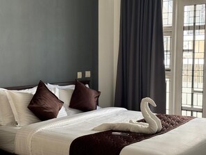A hotel room with a neatly made bed, a swan-shaped pillow, and a window with a view of buildings.