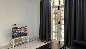 A living room with a television on a stand, a black coffee table, a sofa, and a window with curtains.