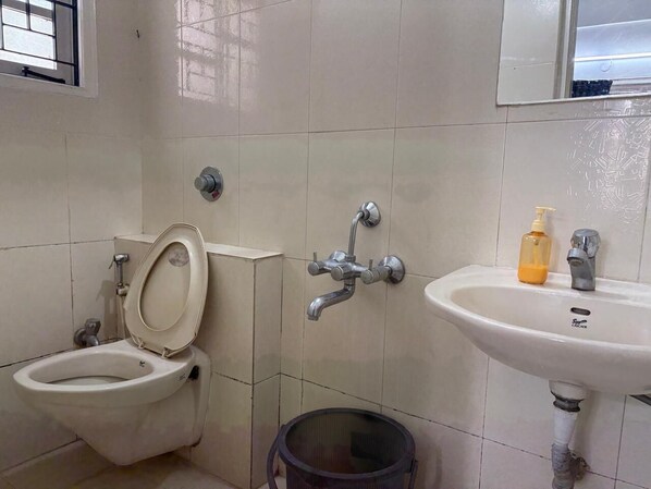 A bathroom with a toilet, a bidet, a sink, and a trash bin.