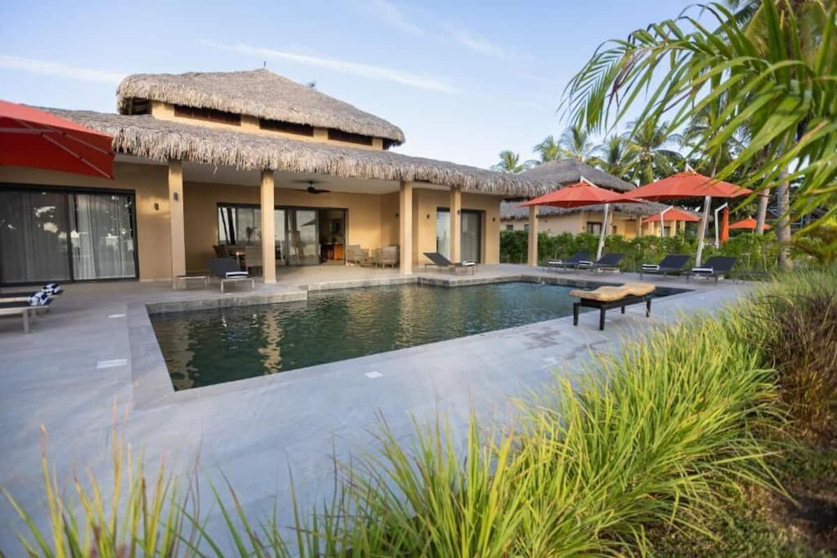 A resort with a swimming pool, thatched-roof structures, and lounge chairs.