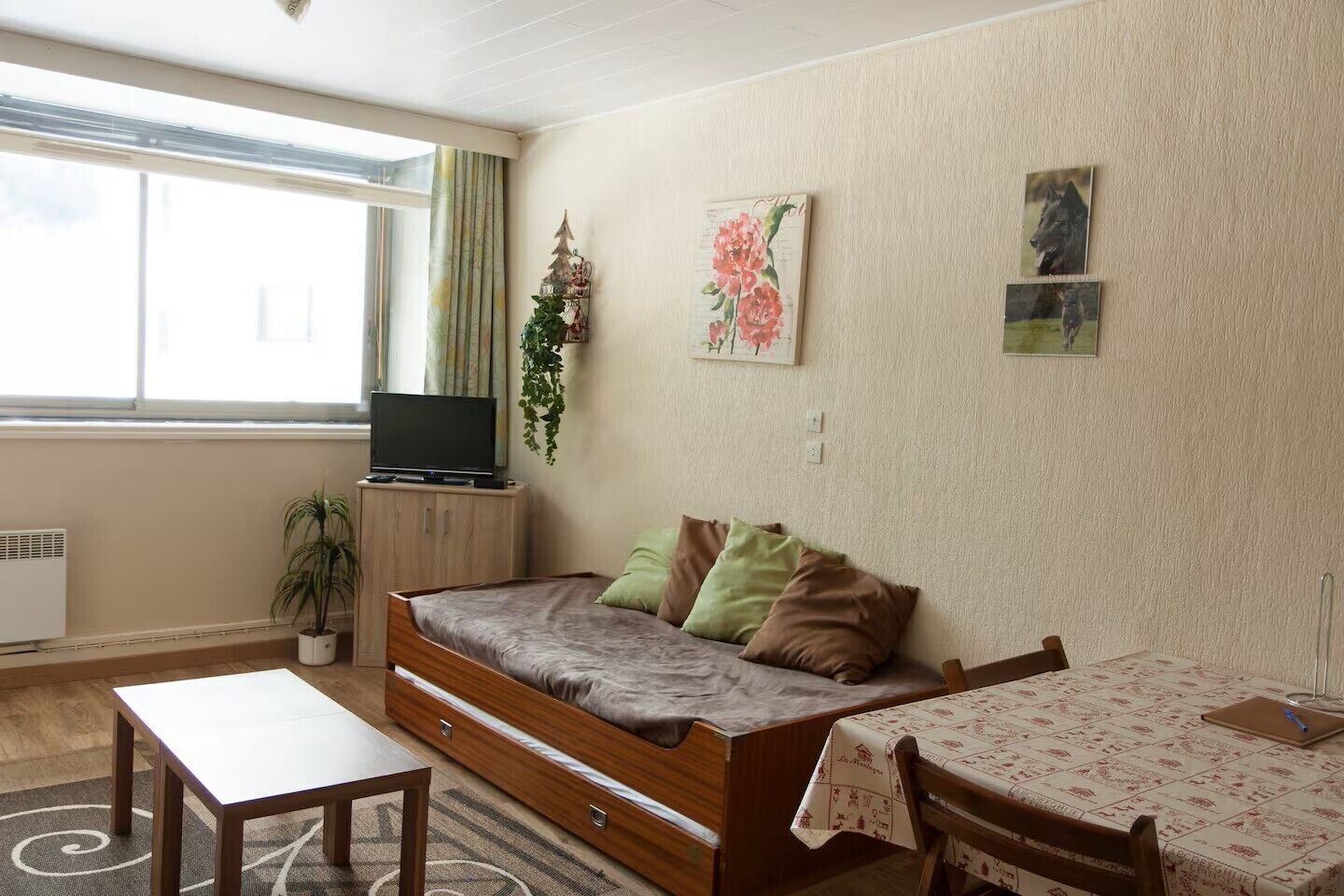 A cozy living room with a sofa, a TV on a cabinet, a small table, and a window with curtains.