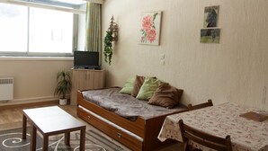 A cozy living room with a sofa, a TV on a cabinet, a small table, and a window with curtains.
