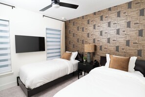 Ein modernes Schlafzimmer mit zwei Betten, einem Deckenventilator, einem an der Wand montierten Fernseher und Tapete mit Muster.