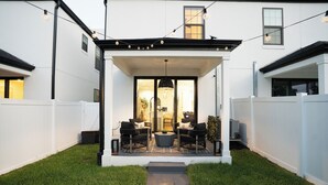 A modern patio with two sofas and a coffee table, surrounded by a white fence and a well-maintained lawn.