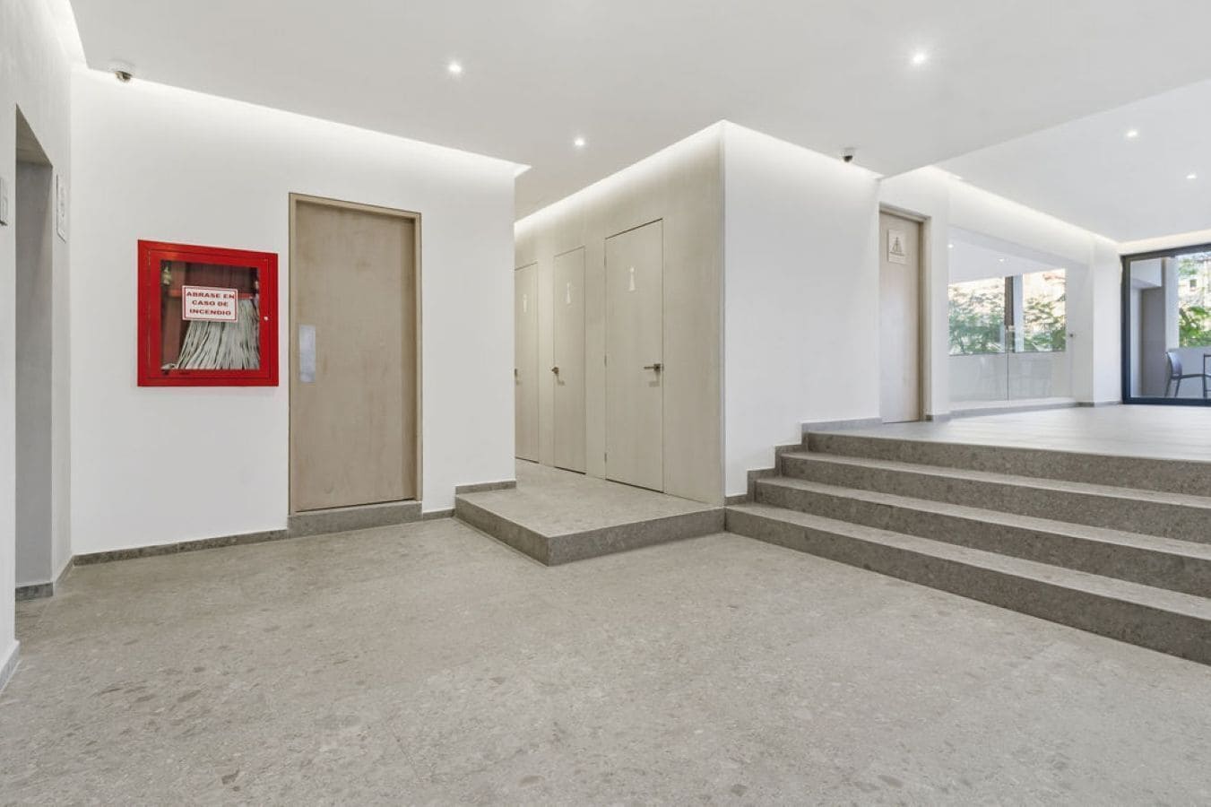 A modern interior with a staircase leading to a second floor, a fire alarm on the left, and a door with a light switch.