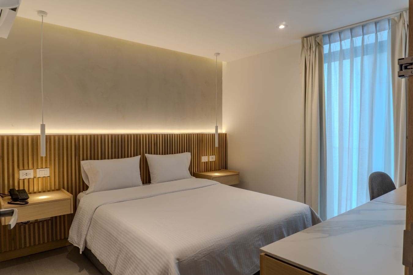 A modern hotel room with a large bed, bedside tables, a desk, and a window with curtains.