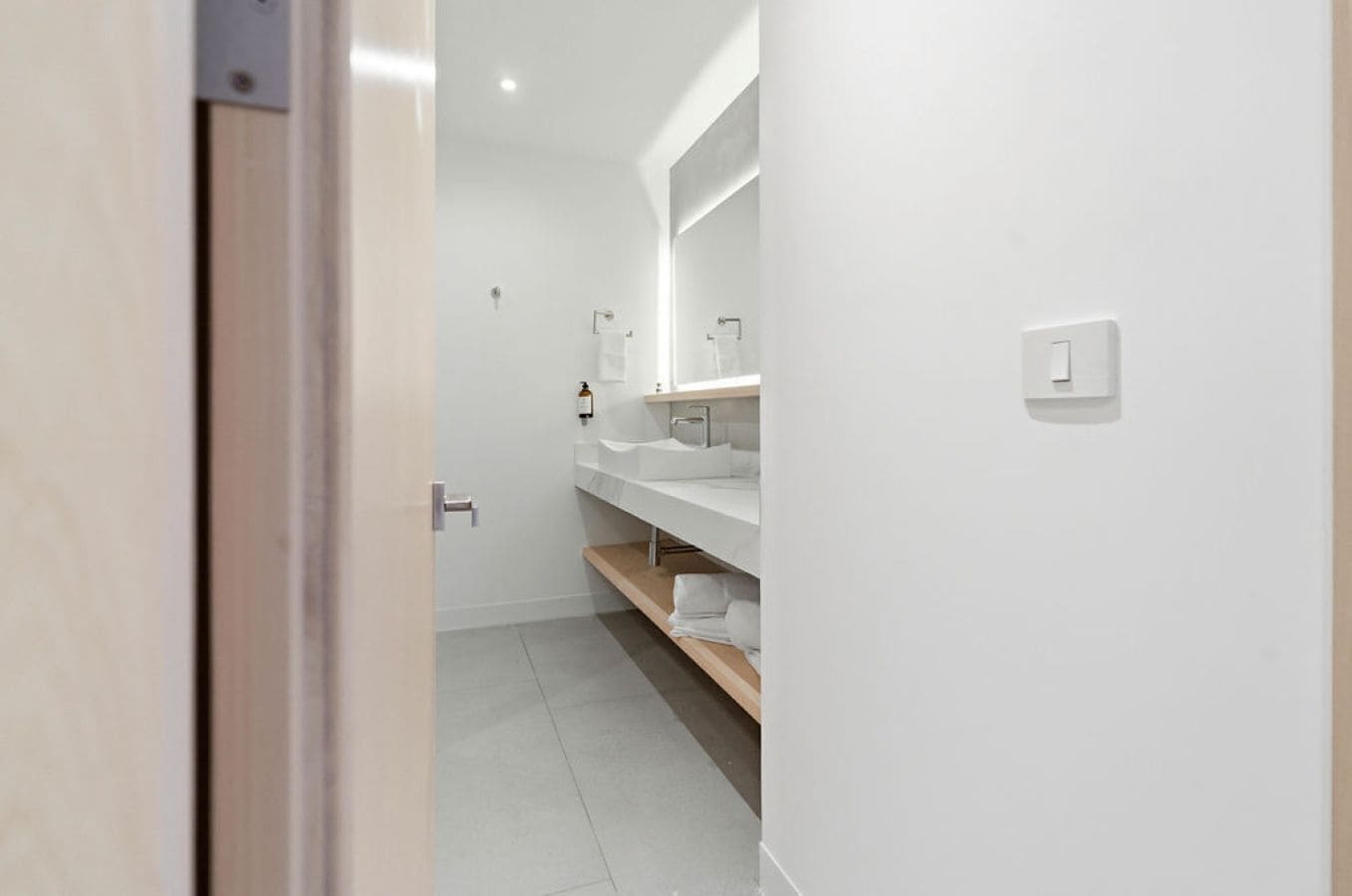 A modern bathroom with a white sink, mirror, and shelves.