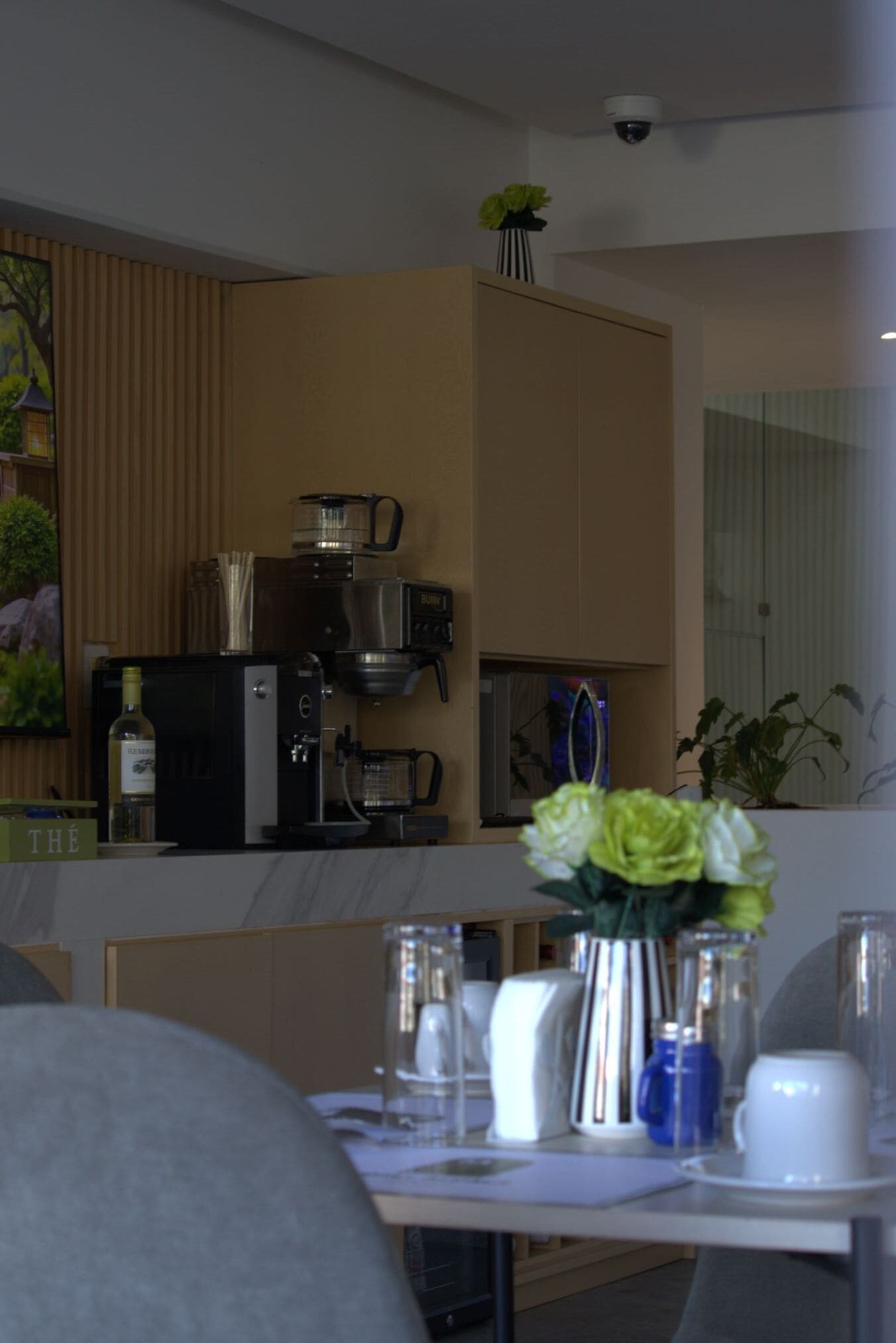 A modern kitchen with a coffee machine, a bottle of wine, and a vase with flowers on the counter.