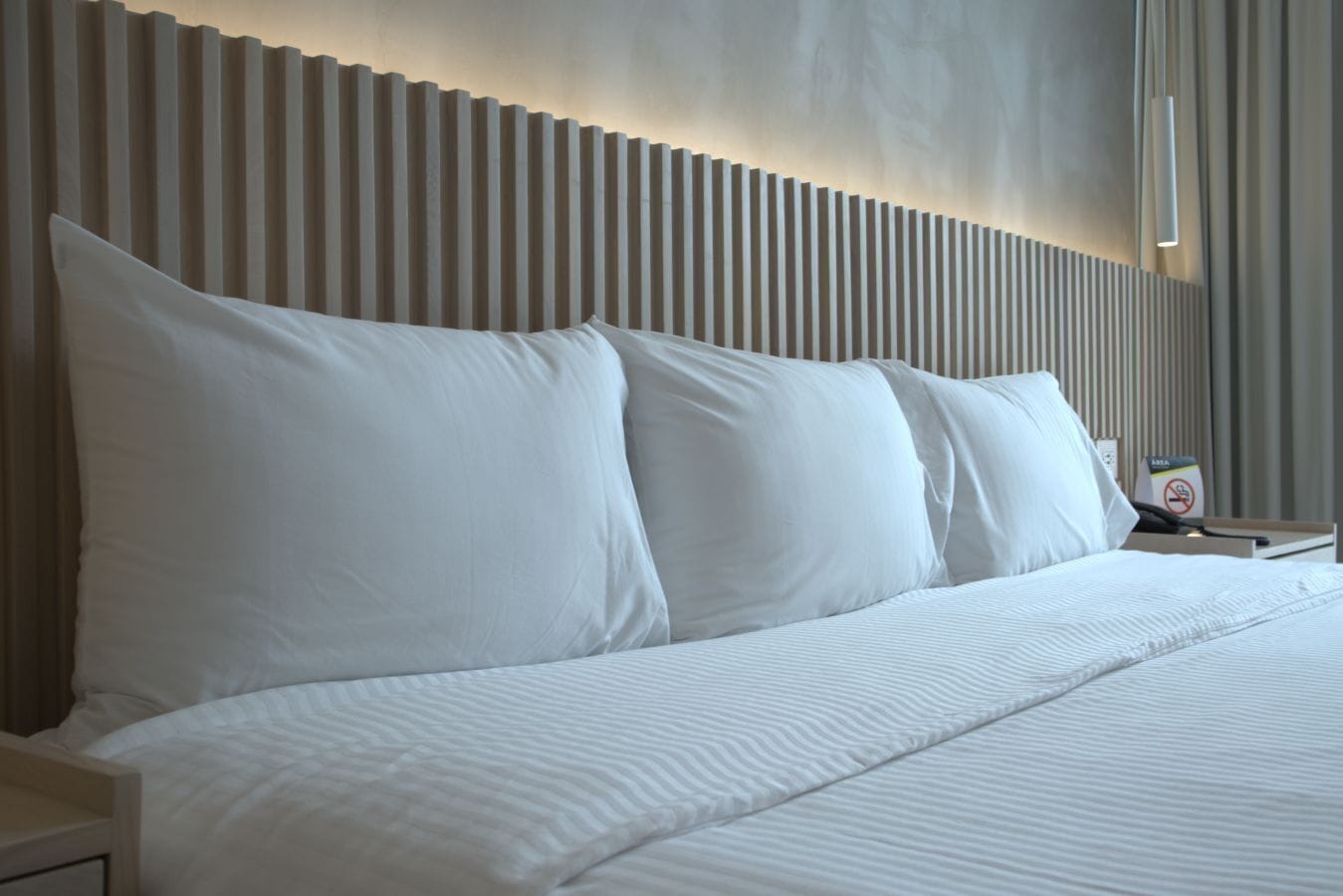 Une chambre d’hôtel avec un grand lit, du linge de lit blanc et une tête de lit moderne dotée de lattes verticales.