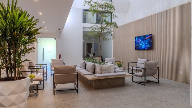 A modern lobby with a sofa, chairs, a coffee table, a large TV, and a potted plant. - Hotel Alcalà Centro (Guadalajara)