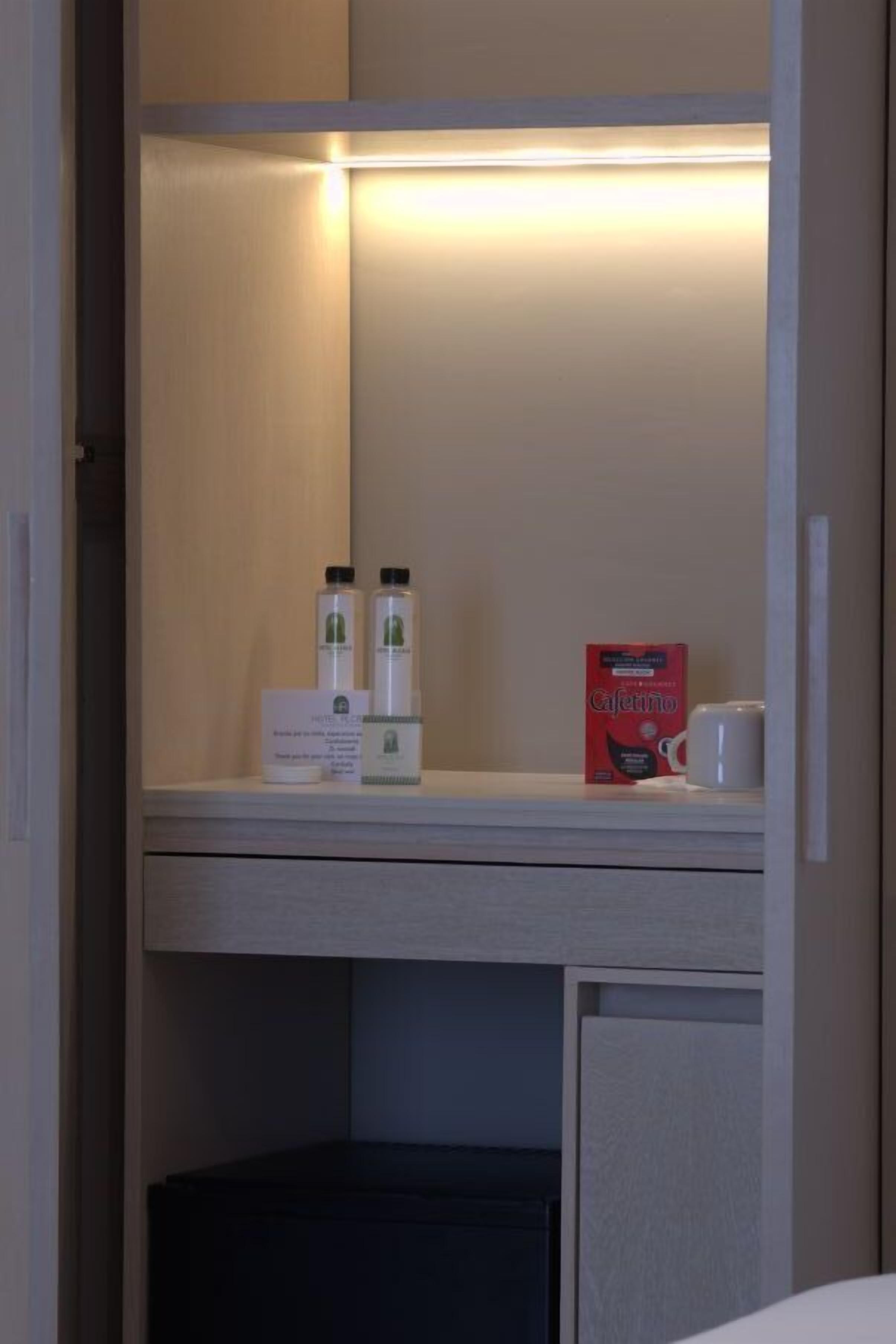 Un mini-bar d’hôtel avec un miroir, une boîte de chocolats au café, deux bouteilles d’eau et une tasse à café.