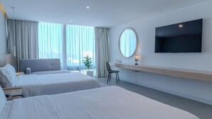 A modern hotel room with two beds, a desk, a chair, a TV, and large windows with curtains. - Hotel Alcalà Centro (Guadalajara)