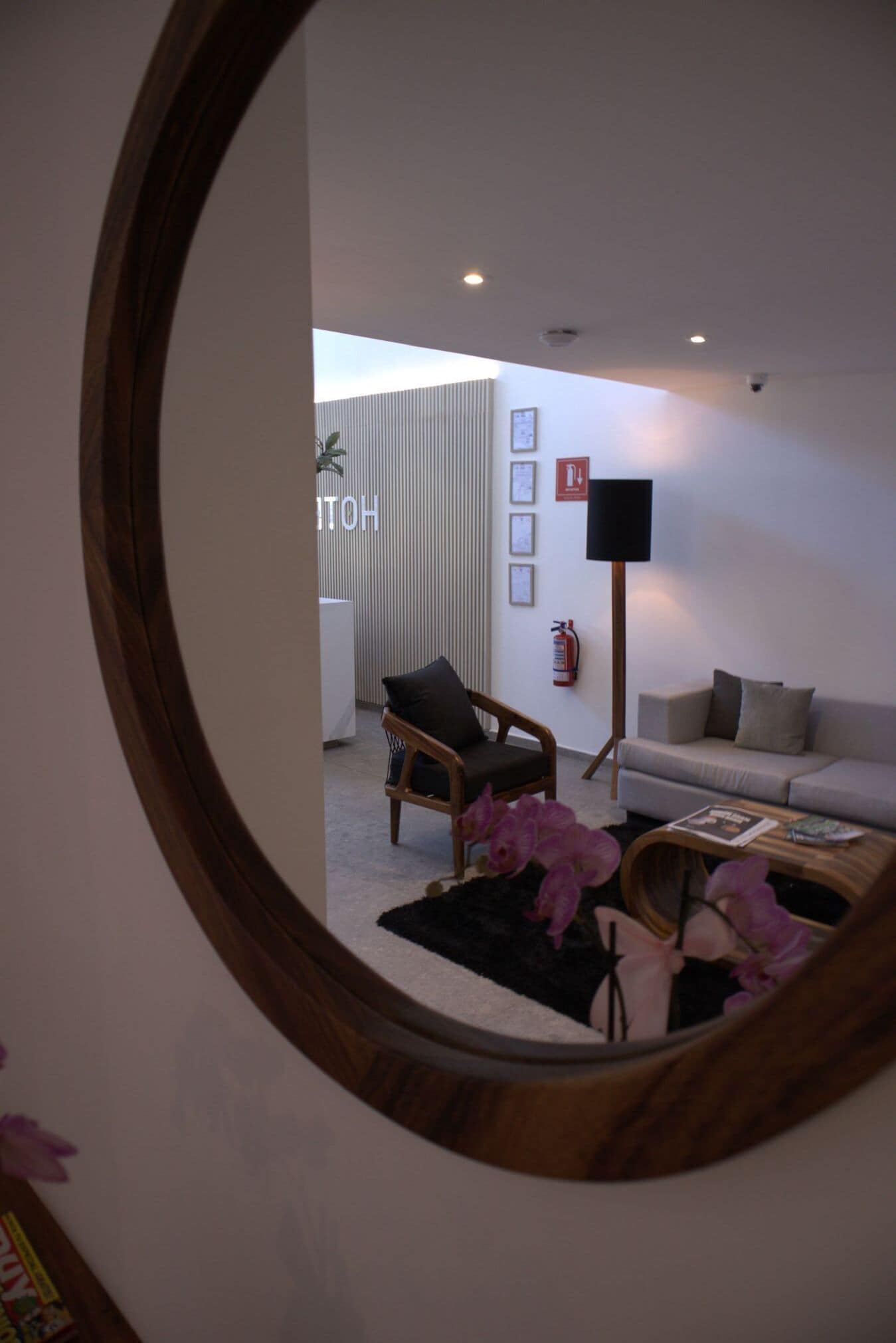 A modern living room with a sofa, armchair, and coffee table, a mirror reflecting the room, and a wall-mounted fire extinguisher.