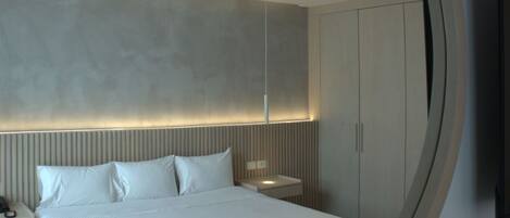 A modern bedroom with a large circular mirror, a bed with white linens, a bedside table, and a wardrobe.